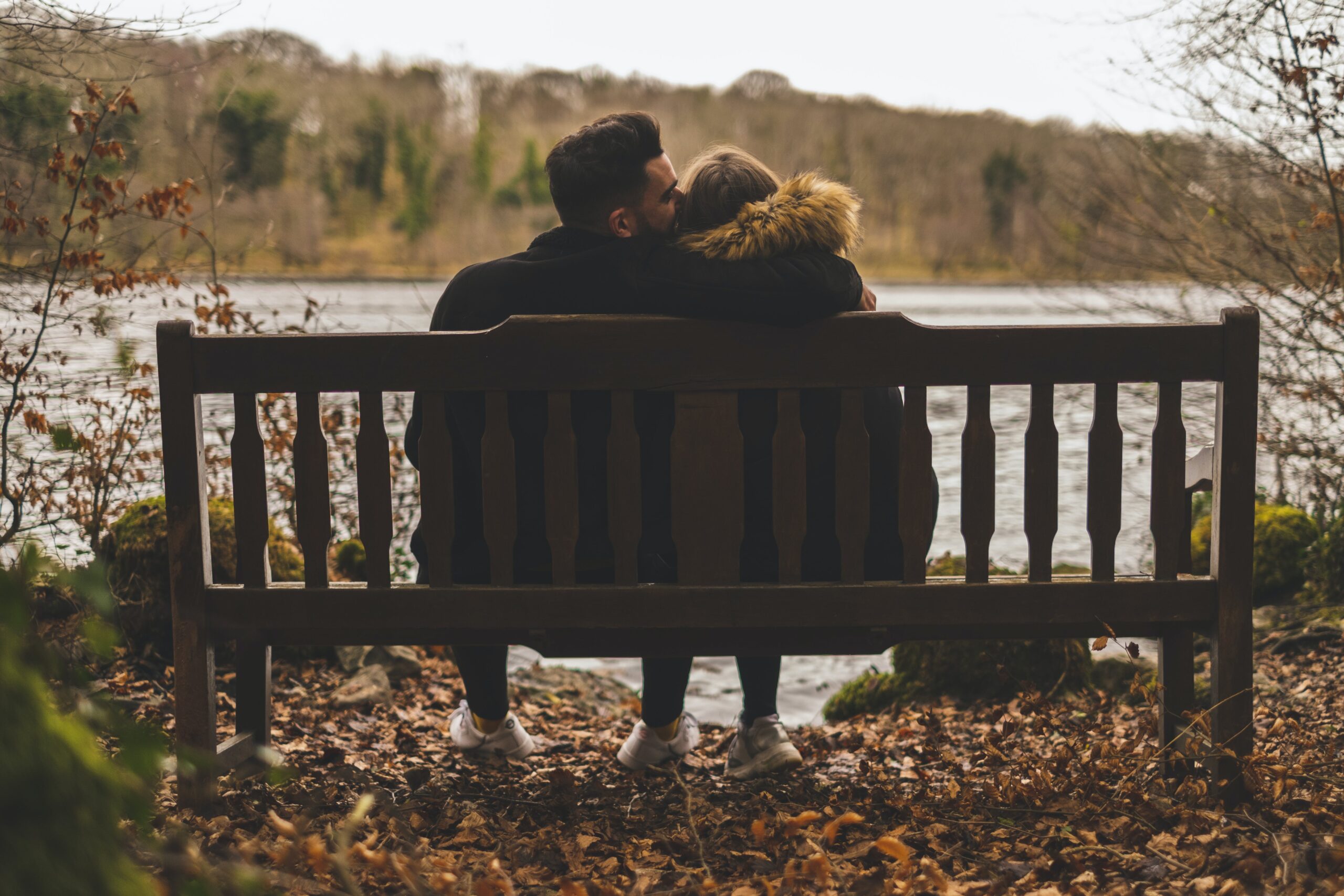 man showing emotional support to his partner on a bench overlooking the water