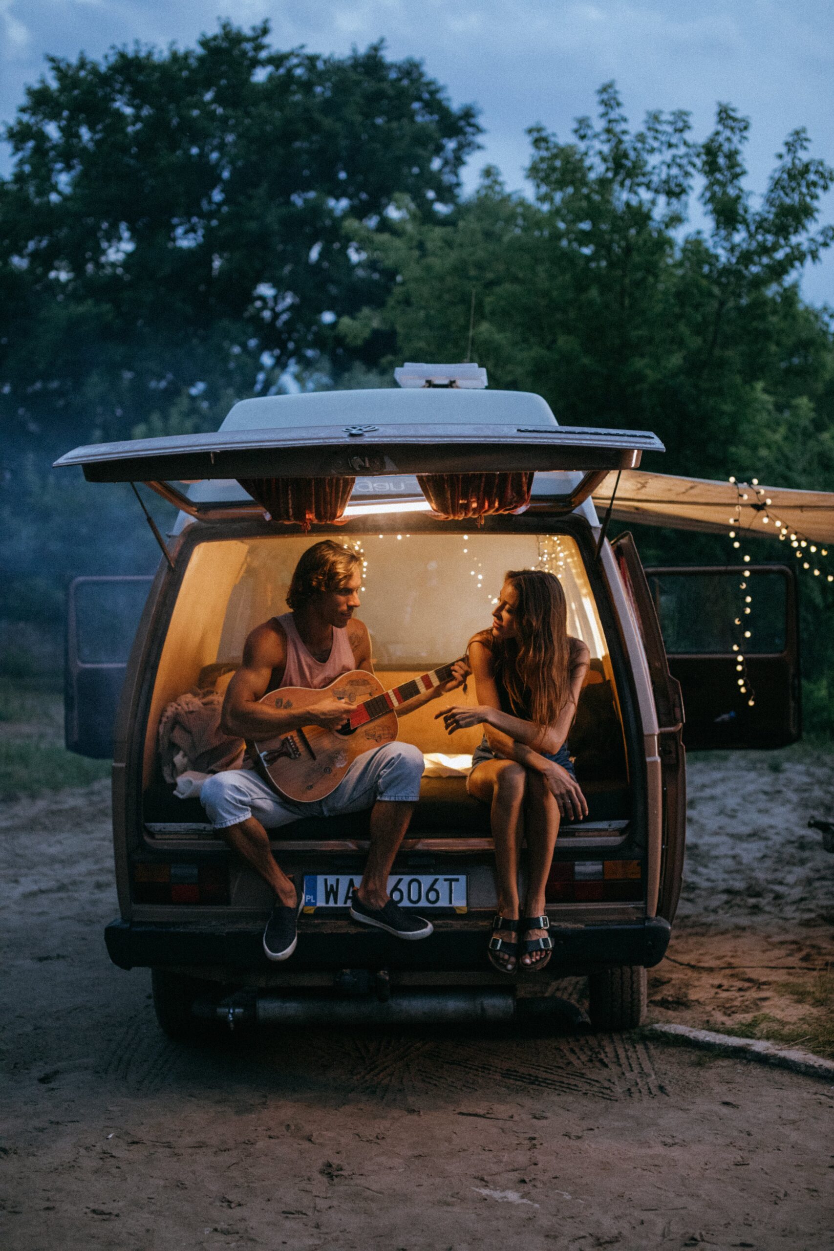 man playing guitar singing to his girlfriend in the back of their vehicle