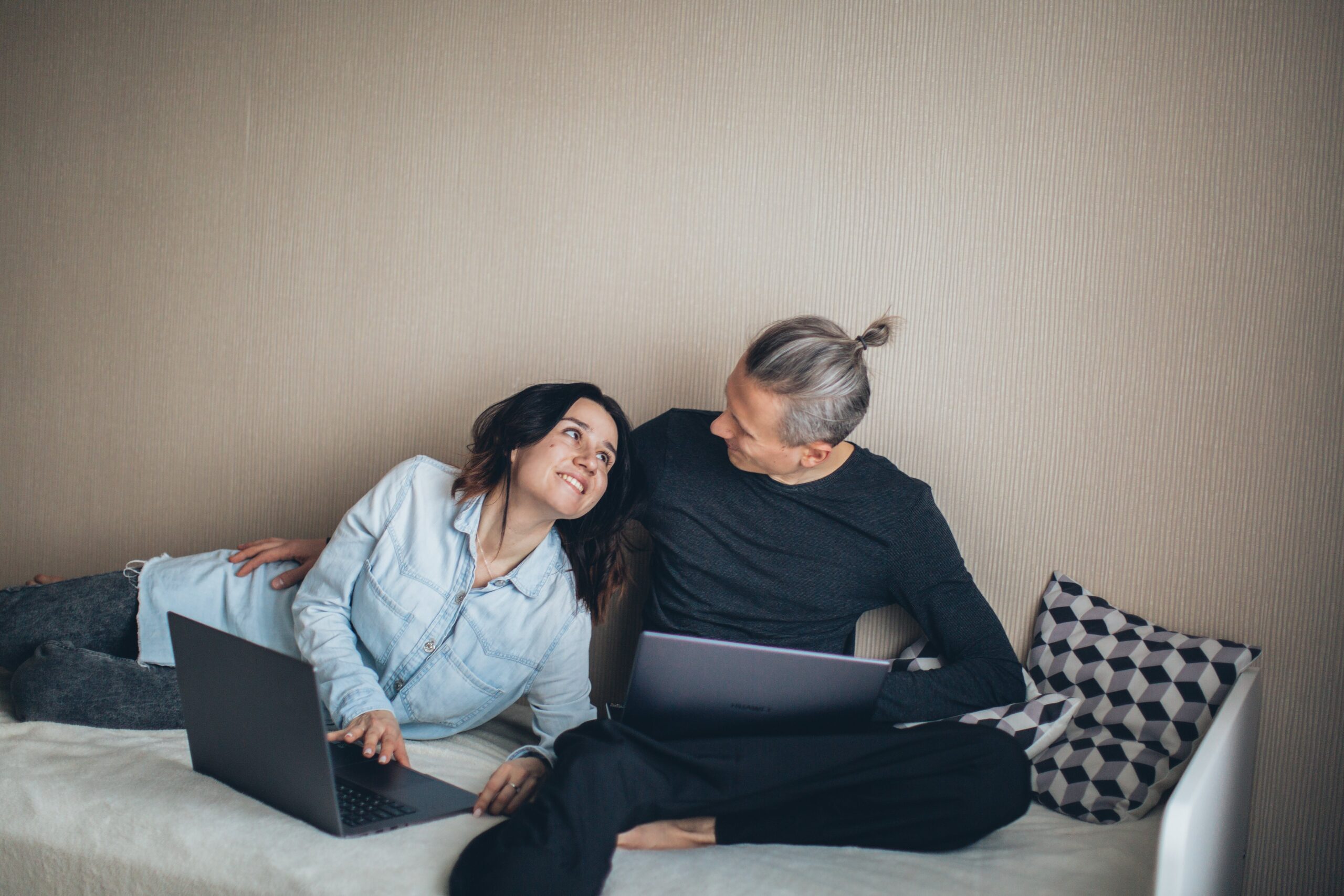 Balancing work and love. Man and woman sitting together on a couch, working on their laptops but still sharing some smiles and laughter.