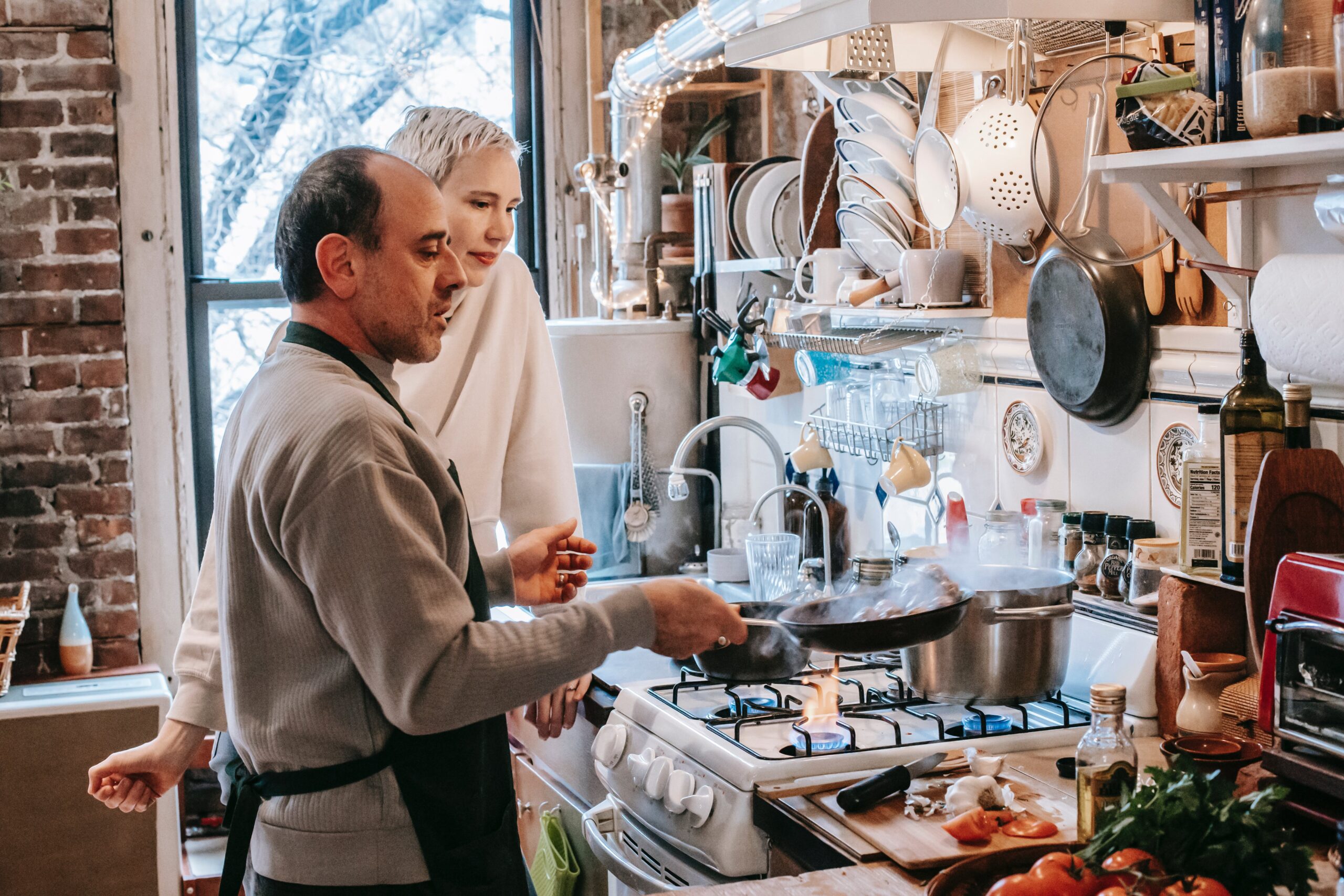 A couple cooking together in the kitchen, surrounded by ingredients and cooking utensils.